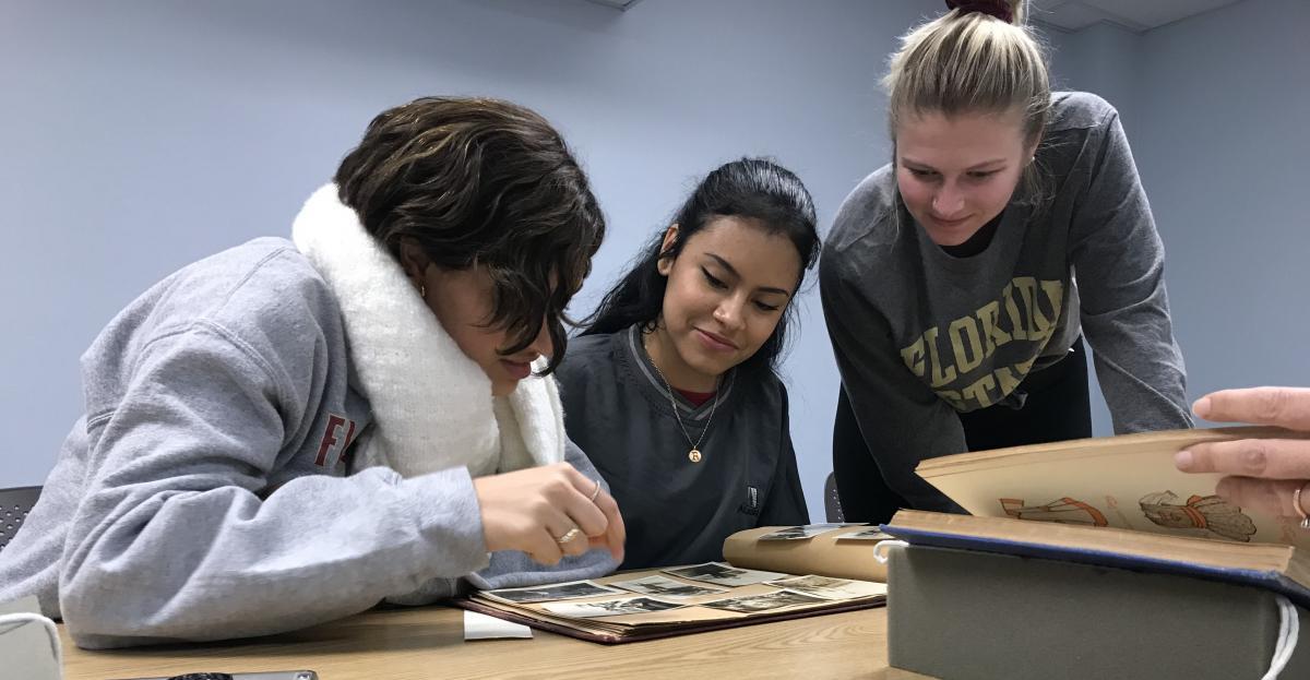 Three patrons look over pictures in a photo album