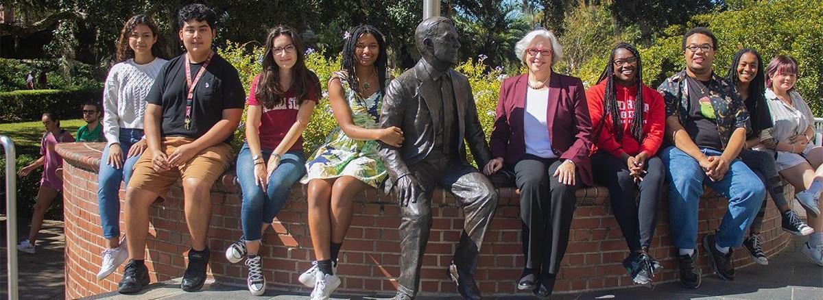 A group of people sit next to the Paul Dirac statue outside FSU Strozier Library