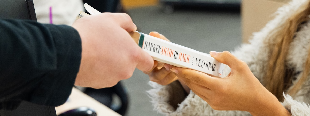 Library user handing book to be checked out to employee working the circulation desk