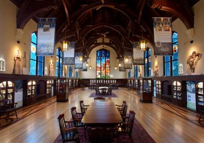 A picture of the interior of the heritage museum with long tables for studying, and very high arched ceiling. Stained glass windows line the sides and back of the room. 