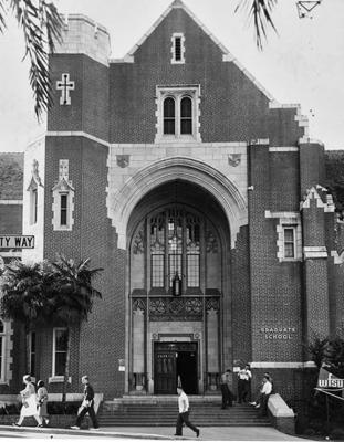 Exterior of Dodd hall in black and white. The front door is covered by a large arch, students walk by outside