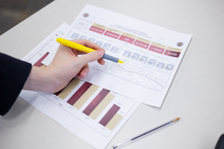 A hand holding a yellow highlighter over a printed paper with bar graphs and text.