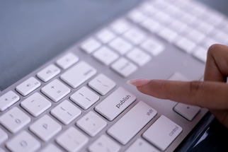 A hand pressing the ‘Publish’ key on a white keyboard.